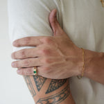 Person with tattoo on arm wearing a gold bracelet and ring, against a white background