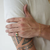 Person with tattoo on arm wearing a gold bracelet and ring, against a white background