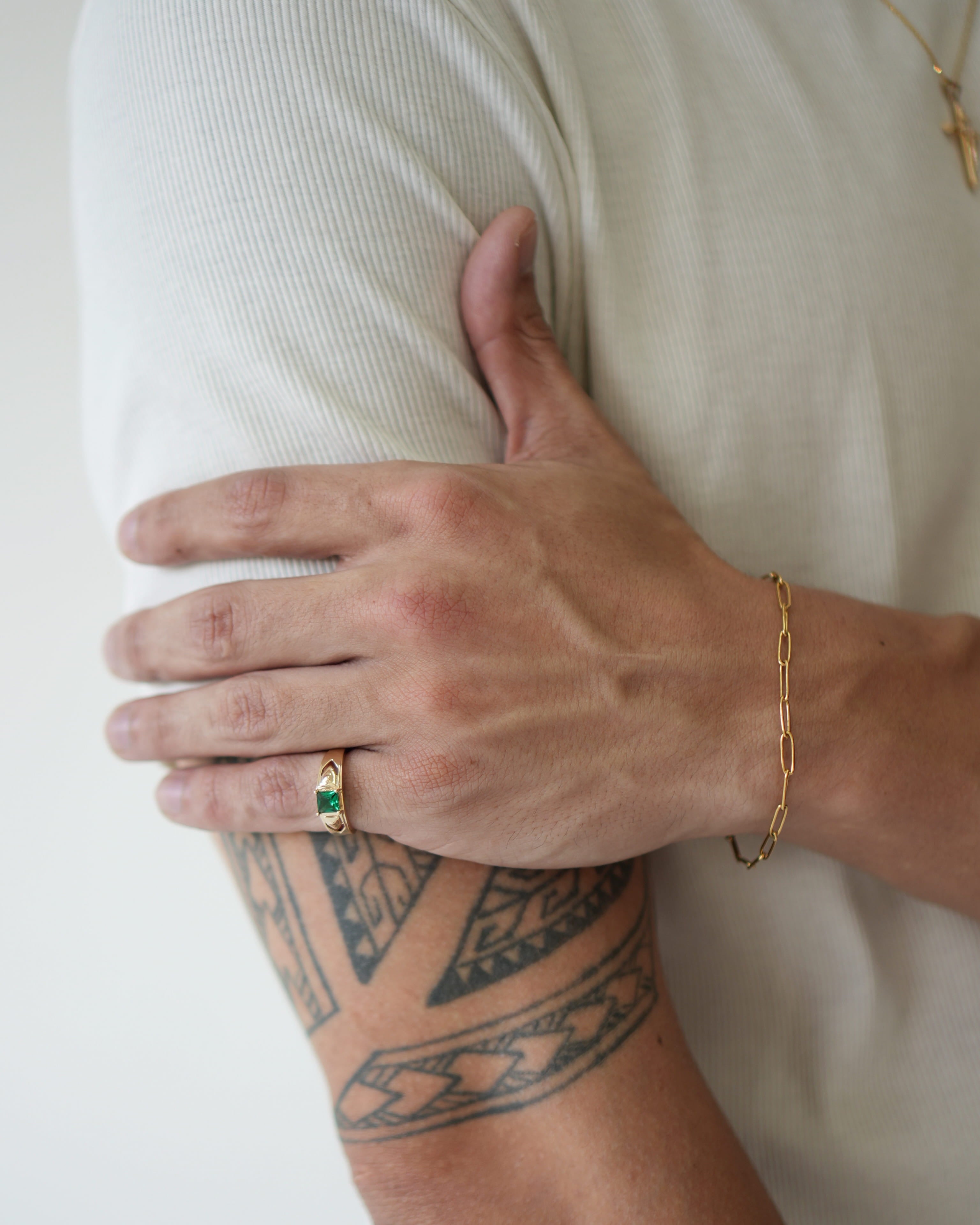 Person with tattoo on arm wearing a gold bracelet and ring, against a white background