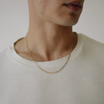 Close-up of a person wearing a gold necklace against a neutral background