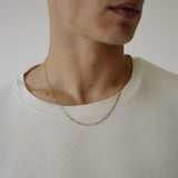 Close-up of a person wearing a gold necklace against a neutral background