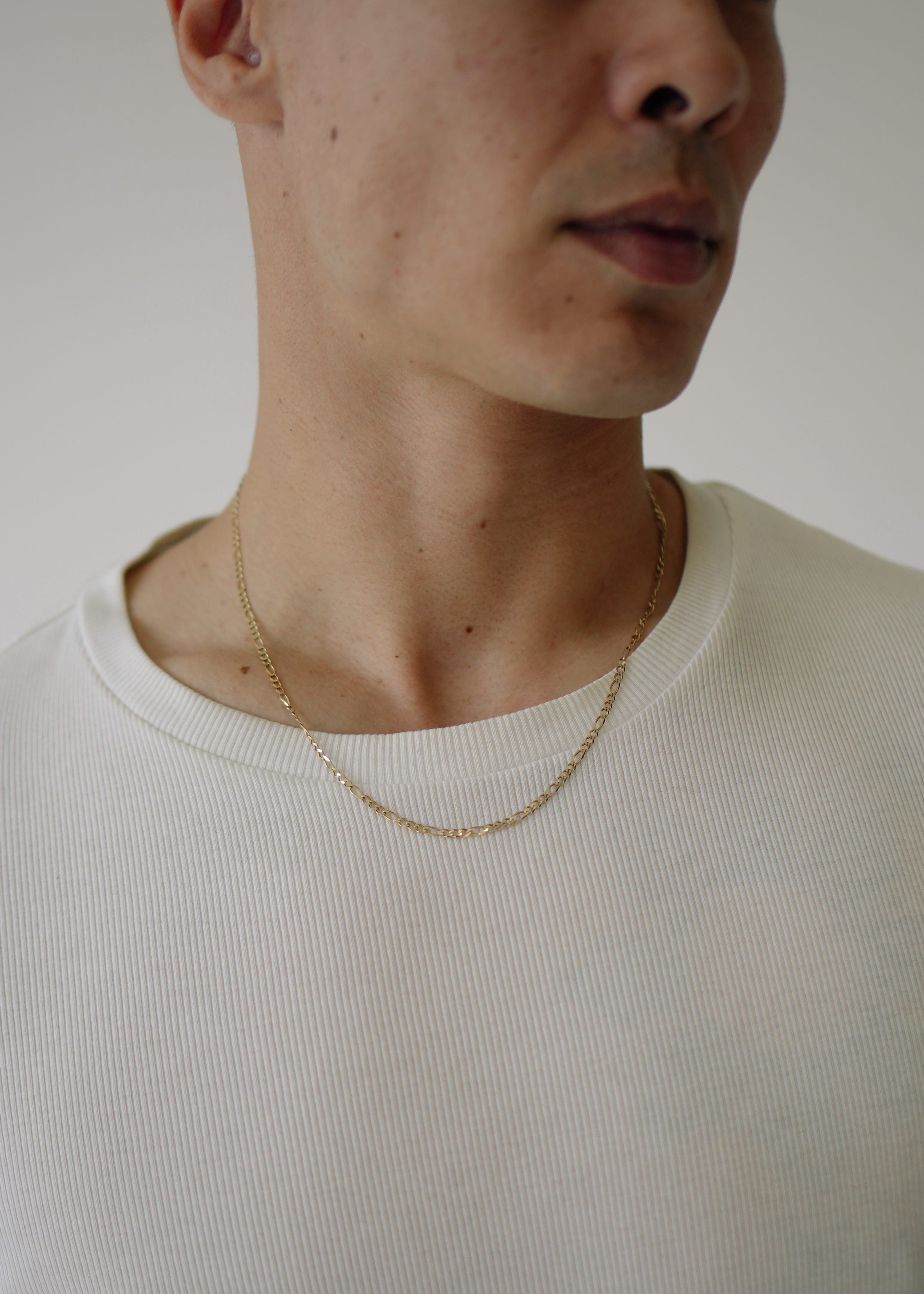 Close-up of a person wearing a gold necklace against a neutral background