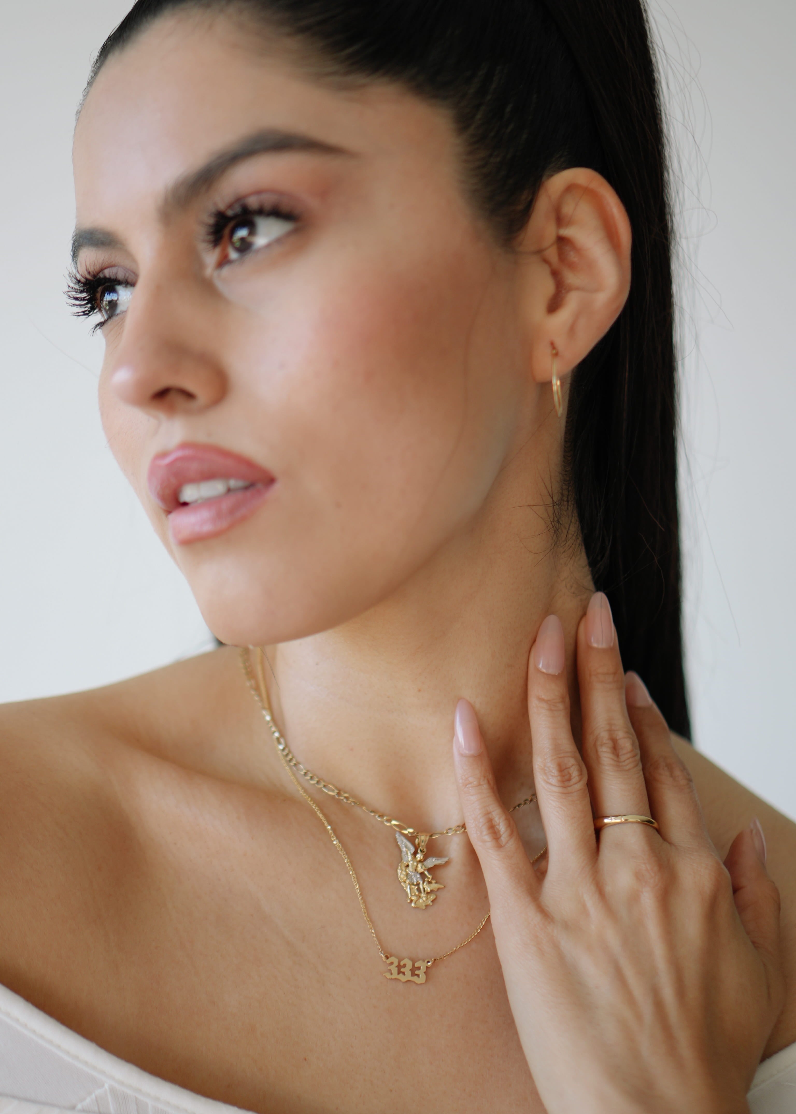 Woman wearing a gold necklace and ring, with a plain background