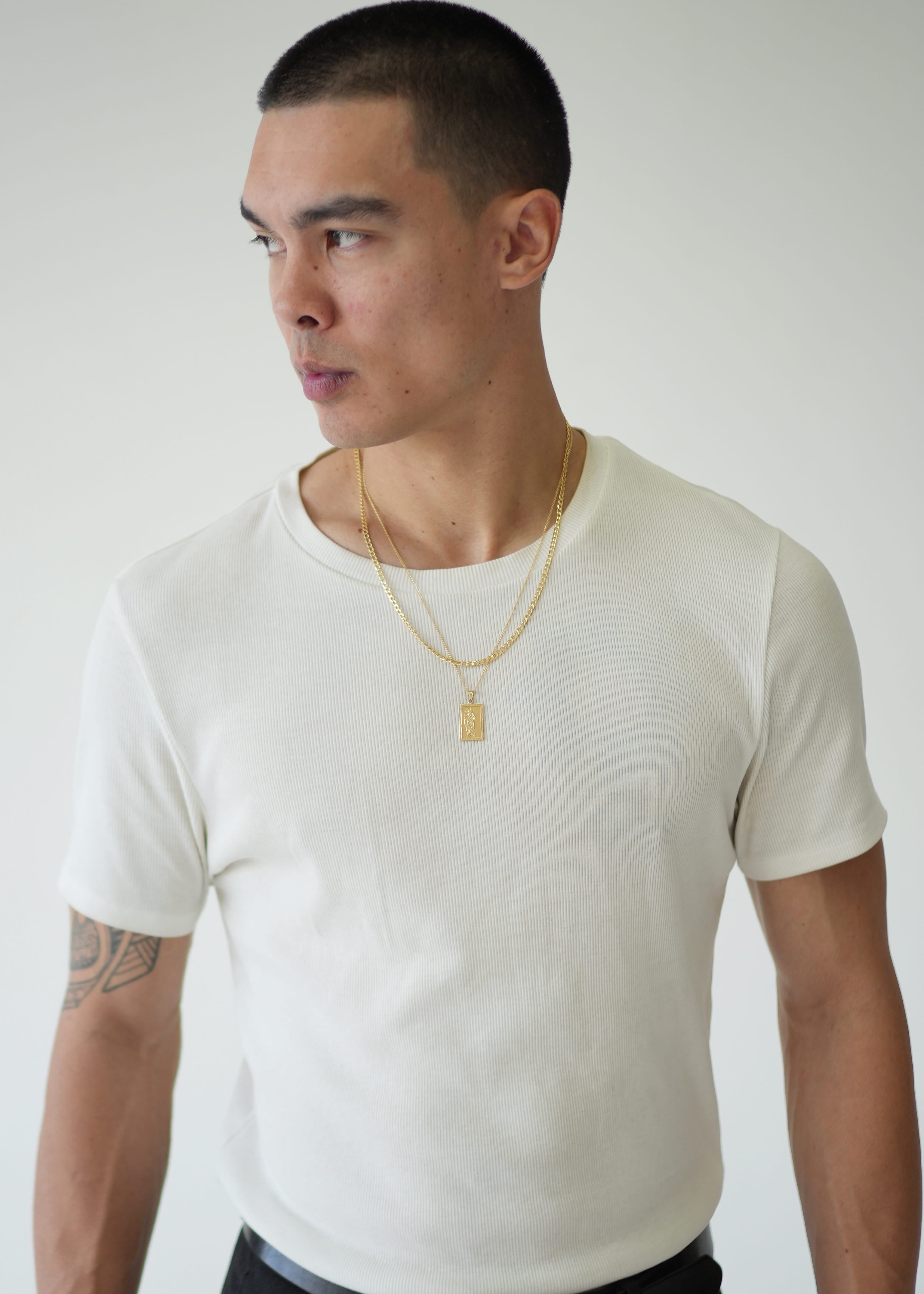 Man wearing a plain white t-shirt and black pants against a light gray background