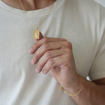 Person wearing a gold necklace and bracelet on a plain background