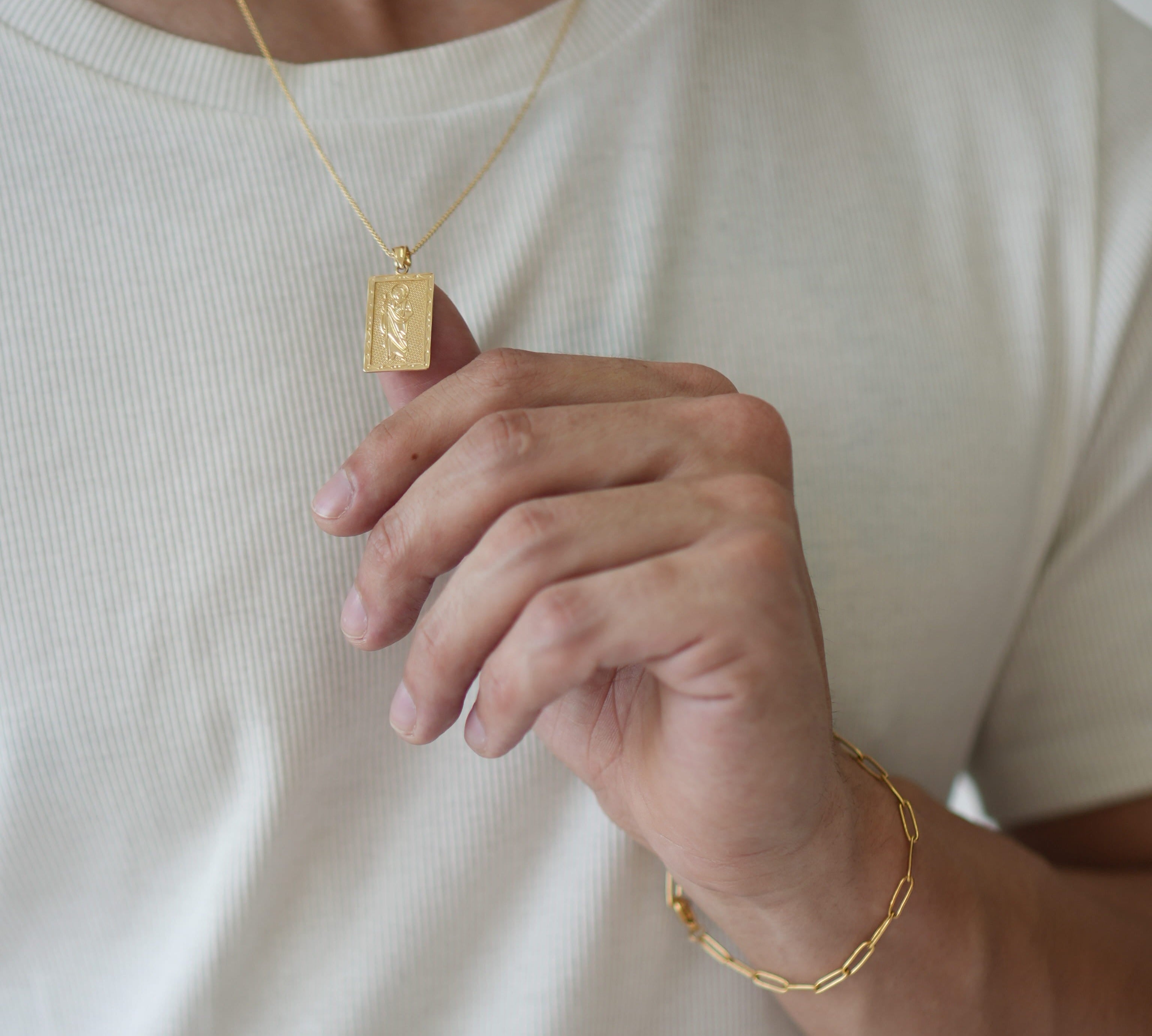 Person wearing a gold necklace and bracelet on a plain background