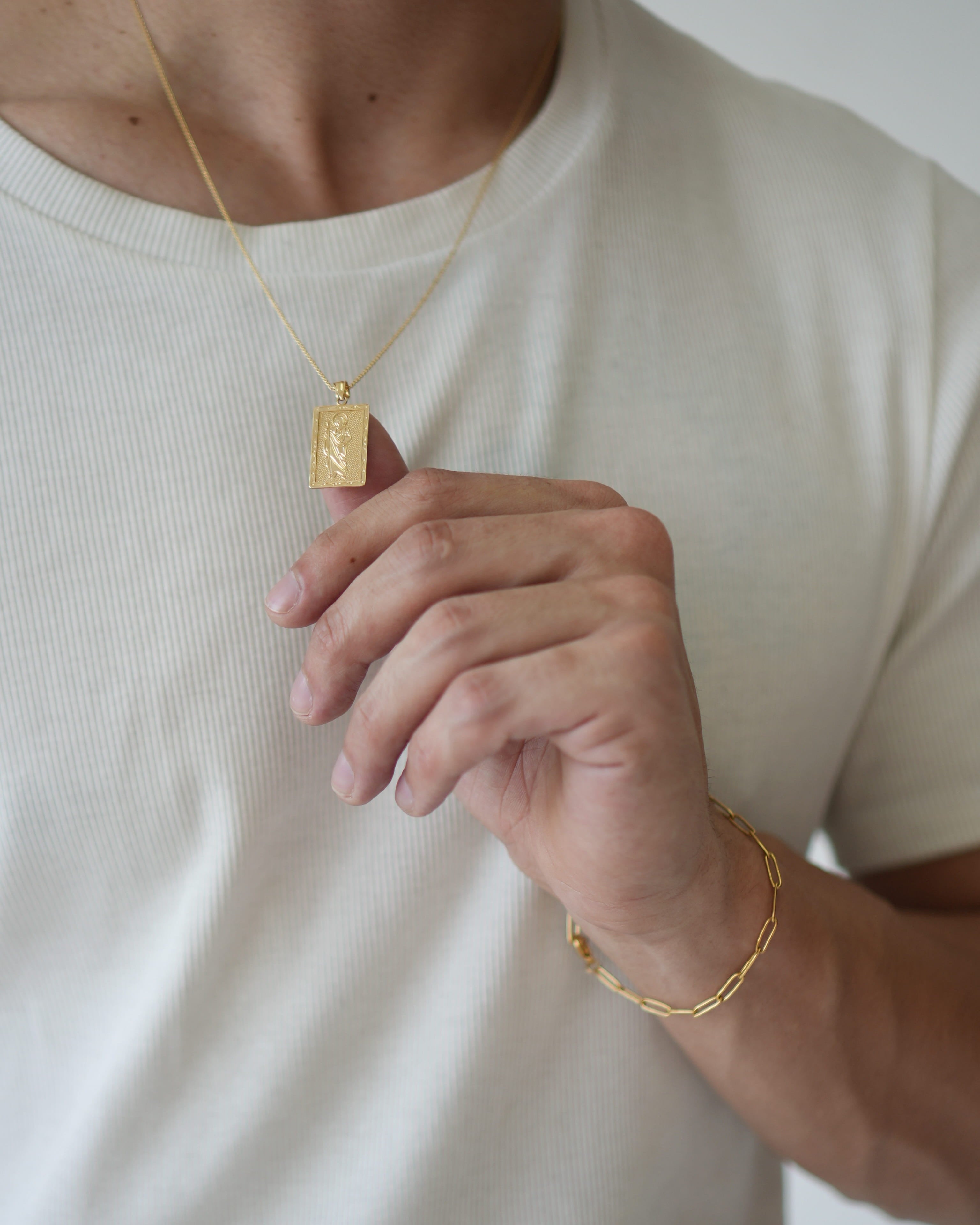 Person wearing a gold necklace and bracelet on a plain background