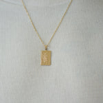 Gold pendant necklace on a person wearing a light gray shirt