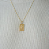 Gold pendant necklace on a person wearing a light gray shirt