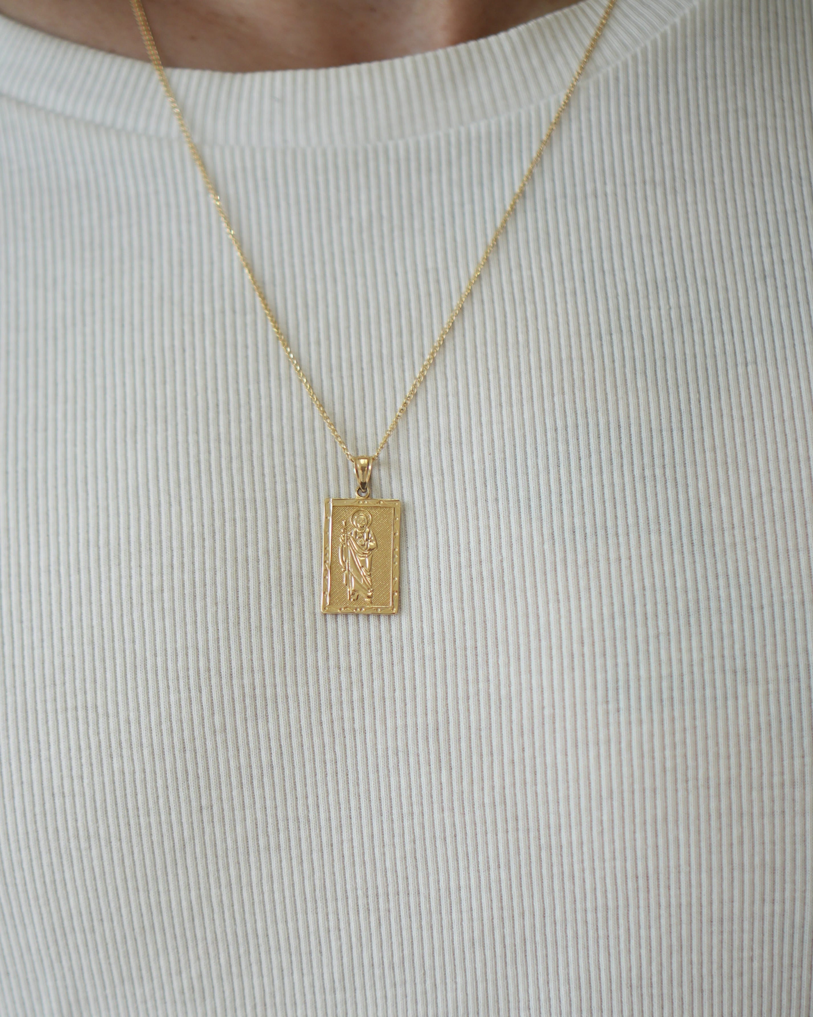 Gold pendant necklace on a person wearing a light gray shirt