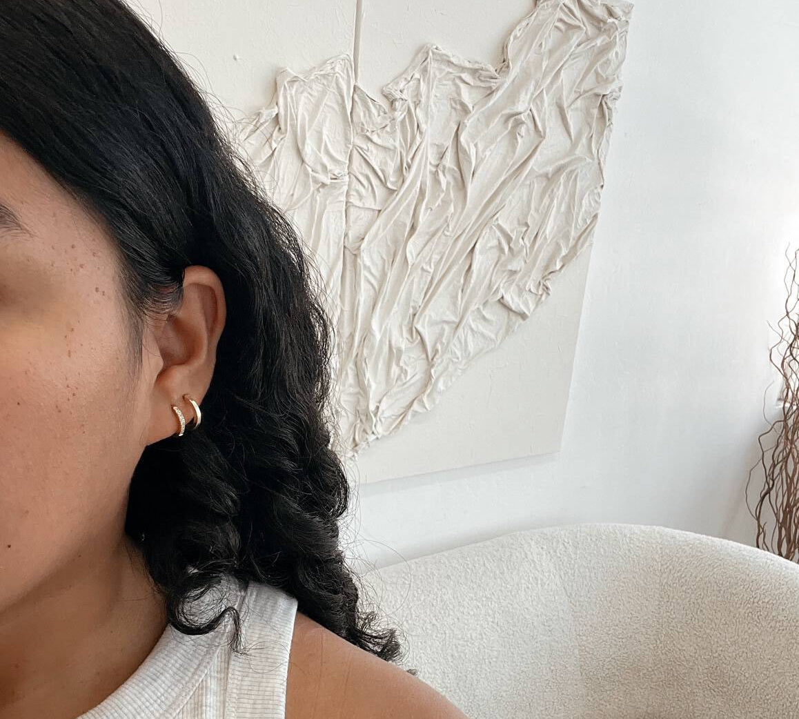 woman taking a selfie with two gold hoops on and a couch in the back