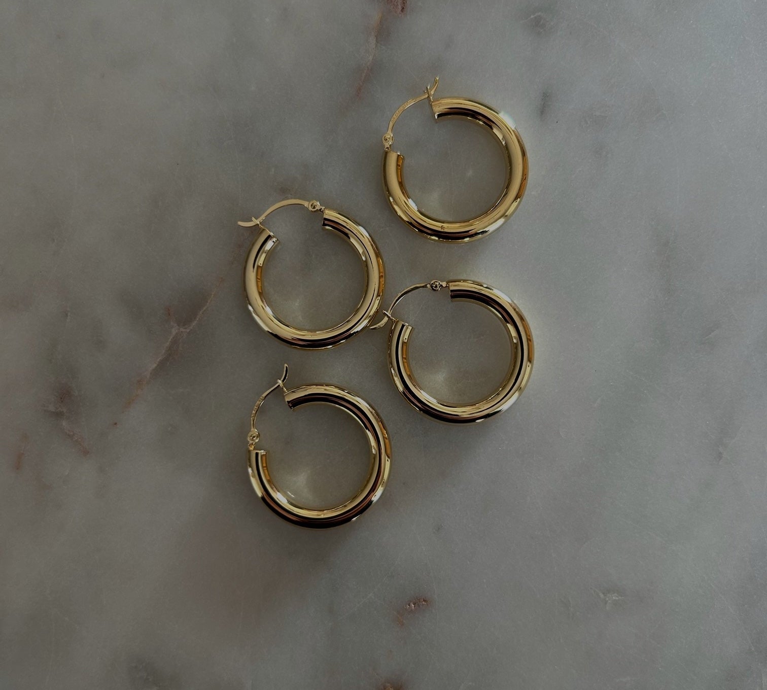 image of four gold hoops in a diagonal pattern on top of a marble table