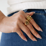 Hand wearing multiple gold rings on a white and blue background