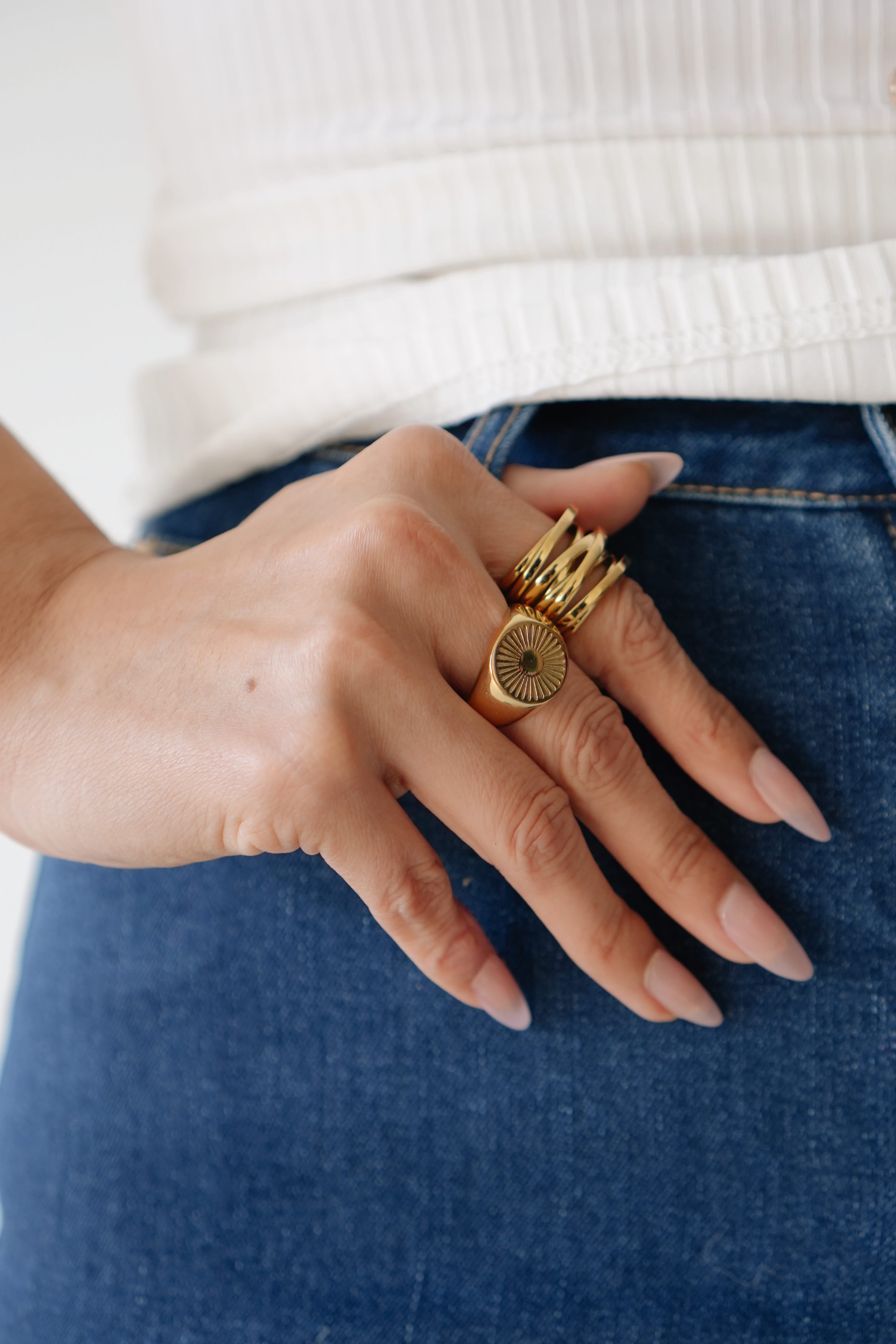 Hand wearing multiple gold rings on a white and blue background